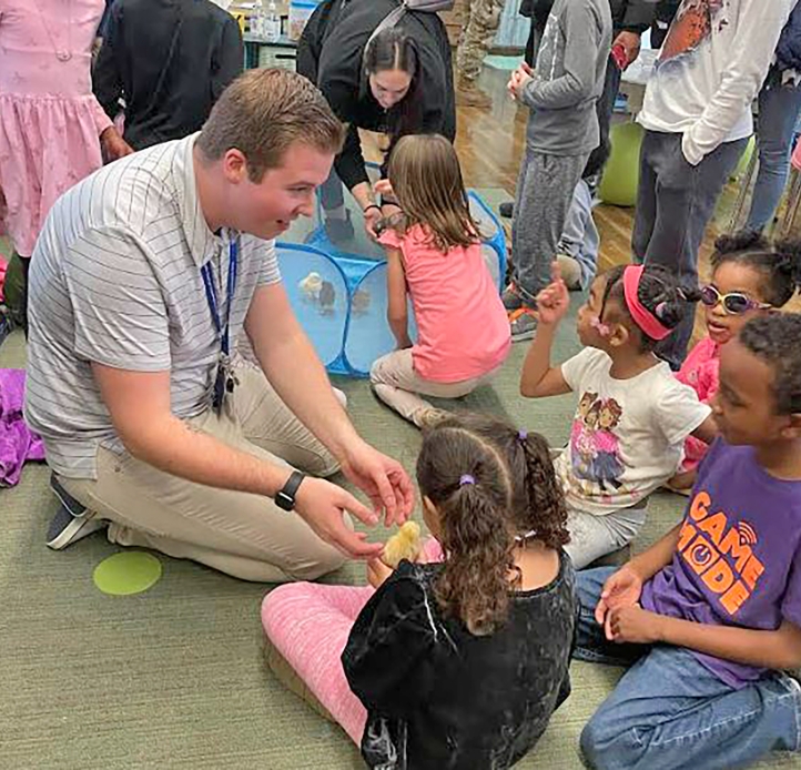 Alex Bianchi kneeling on the floor talking with elementary aged children